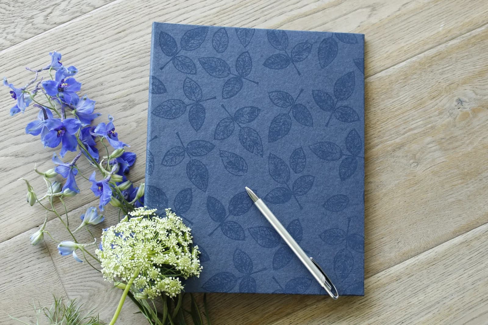 Een blauw notitieboek met een pen, naast een bosje veldbloemen