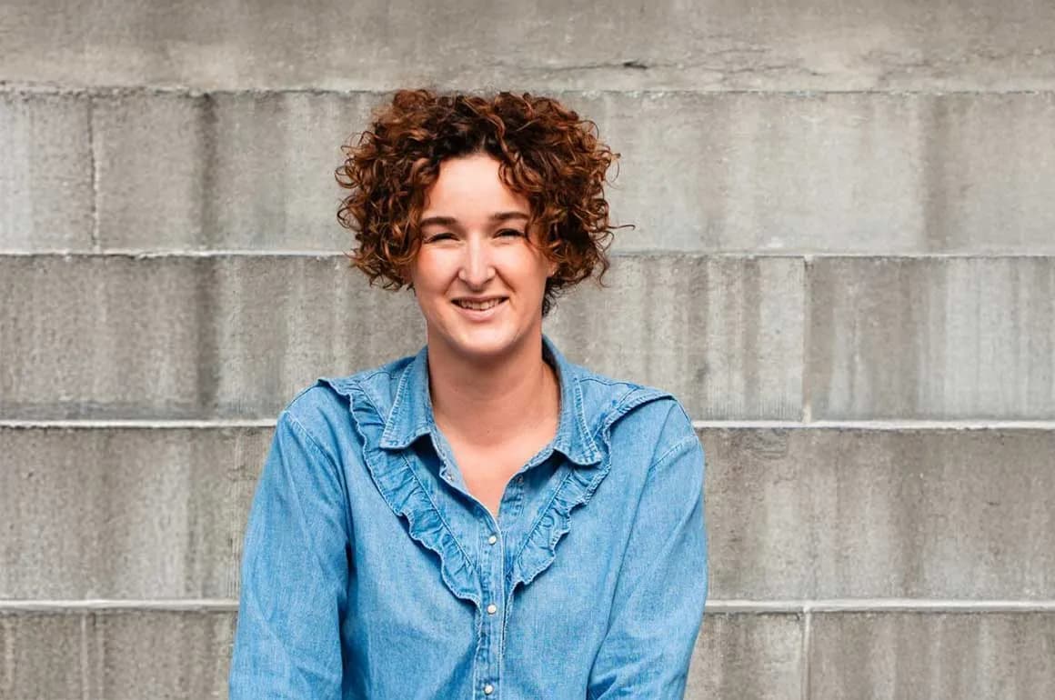 Annemarie Voogt, uitvaartbegeleider, lachend voor een grijze muur