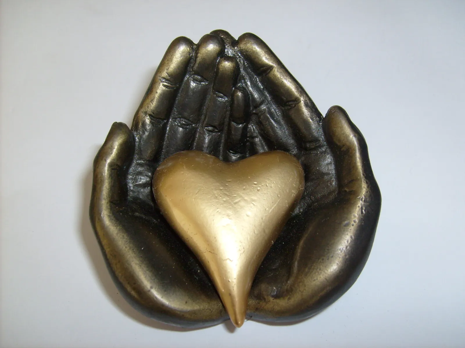 Een bronzen beeldje van twee handen die een gouden hart dragen